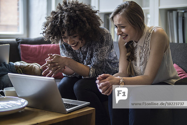 Two happy young women sharing laptop