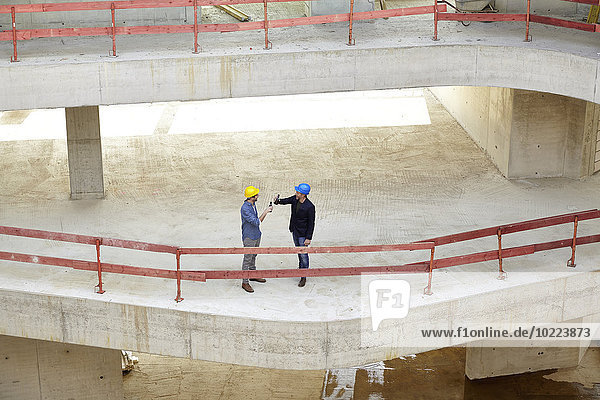 Zwei Männer mit Schutzhelmen die auf der Baustelle klirren.