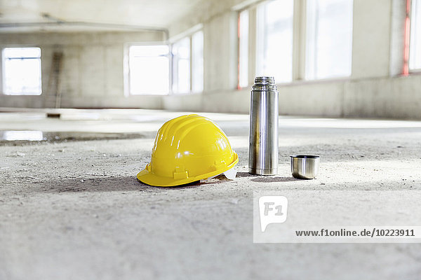 Thermoskanne und Schutzhelm auf Betonboden auf der Baustelle