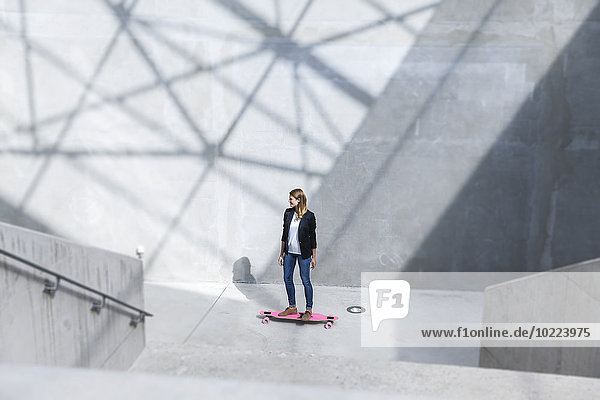 Geschäftsfrau mit rosa Skateboard in moderner Architektur