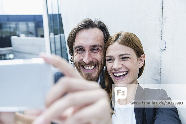 Porträt von zwei lachenden Geschäftsleuten  die einen Selfie mit Smartphone nehmen