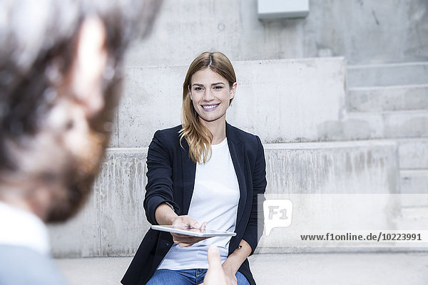 Portrait of smiling businesswoman giving digital tablet to her partner