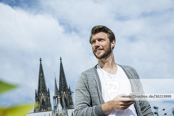 Germany  Cologne  portrait of young man with smartphone hearing music