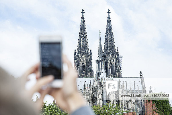 Germany  Cologne  young woman taking a picture of Cologne Cathedral with smartphone