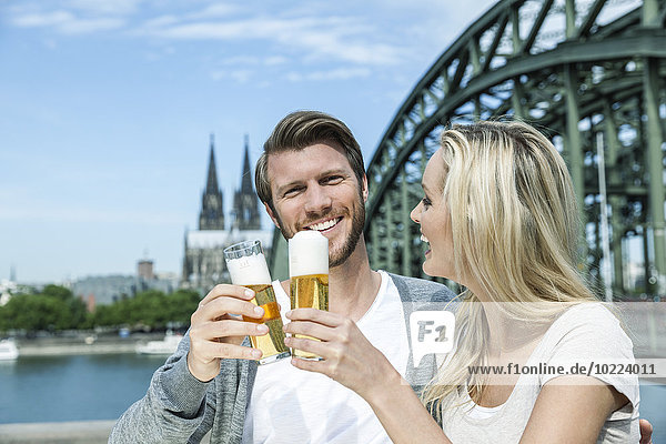Germany  Cologne  happy young couple toasting with Koelsch glasses in front of Rhine River
