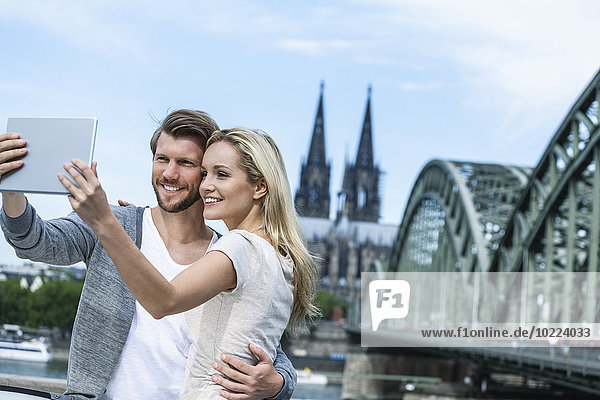 Germany  Cologne  smiling young couple taking a selfie with digital tablet