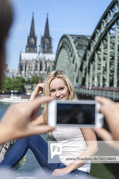 Germany  Cologne  young man taking a picture of his girlfriend with smartphone