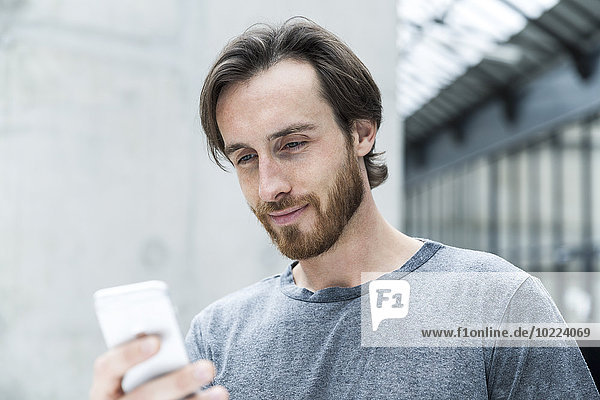 Porträt eines jungen Mannes mit Blick auf sein Smartphone