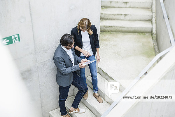 Zwei Geschäftsleute stehen auf einer Treppe und schauen auf ein digitales Tablett.