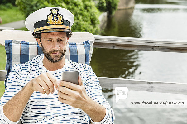 Man wearing captain's hat looking at cell phone