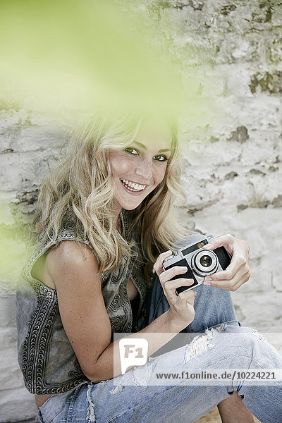 Porträt einer lächelnden blonden Frau mit einer alten Kamera