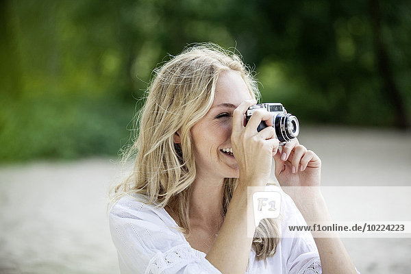 Lächelnde blonde Frau beim Fotografieren mit einer alten Kamera