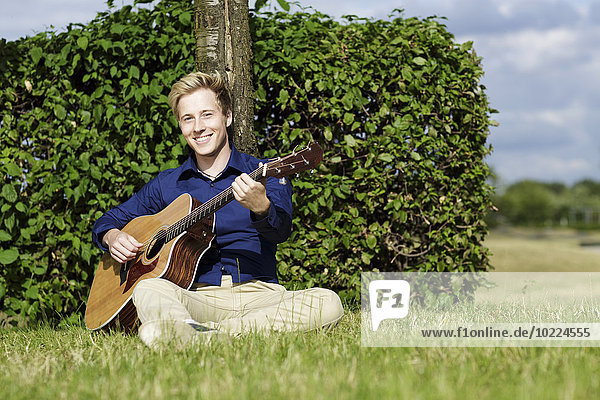 Smiling young man playing guitar in meadow