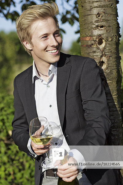 Lächelnder junger Mann im Freien mit Weinglas und Flasche