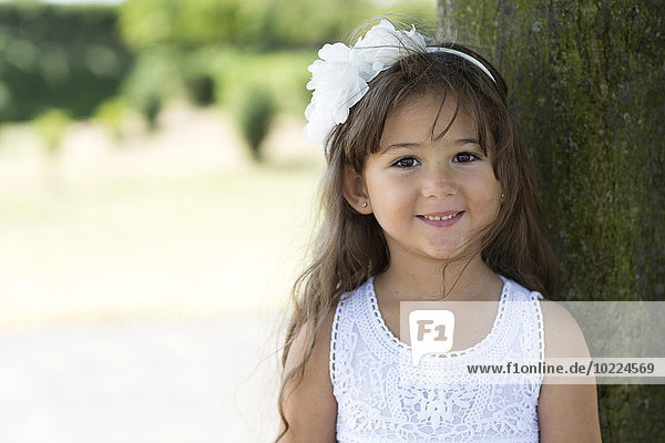 Porträt eines lächelnden kleinen Mädchens  das sich an einen Baum lehnt.