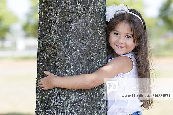 Porträt eines lächelnden kleinen Mädchens  das einen Baum umarmt.