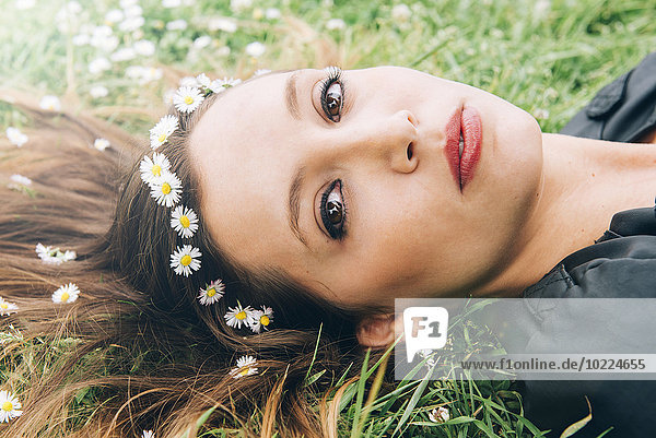Porträt einer jungen Frau auf Gras mit Gänseblümchen im Haar