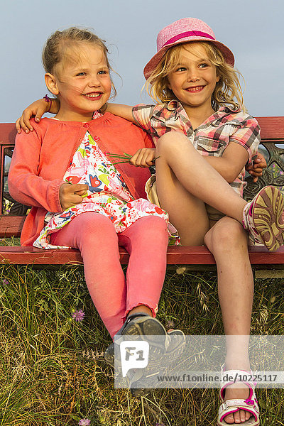 Greece Corfu Afionas two little girls sitting side by side on a bench at evening twilight