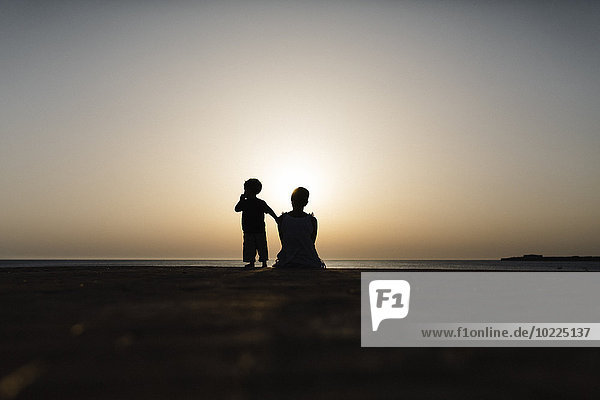Spanien  Menorca  Silhouette von Mutter und Sohn bei Sonnenuntergang am Meer