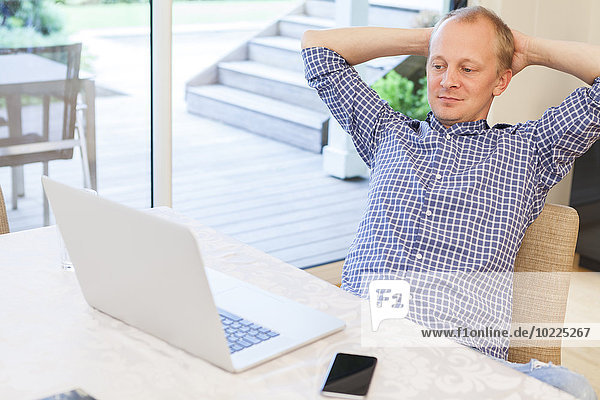 Man with hands behind his head looking at his laptop