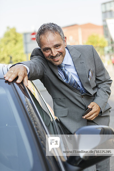 Porträt eines lächelnden Geschäftsmannes  der sich auf das Auto stützt.