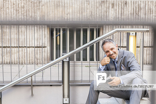 Porträt eines lächelnden Geschäftsmannes im grauen Anzug auf der Treppe