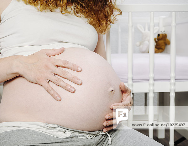 Schwangere Frau vor dem Kinderbett  die ihren Bauch hält