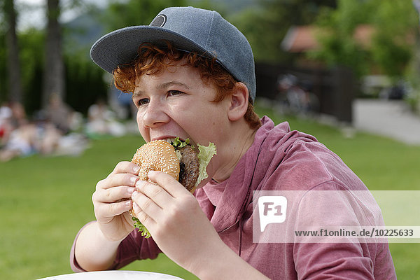 Teenager Junge mit Baseballkappe beim Hamburgeressen