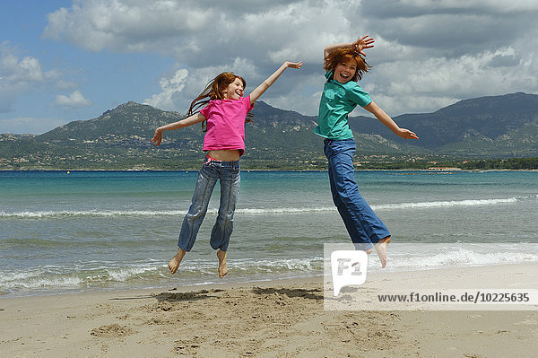 France  Corsica   Calvi  two children jumping in the air on the beach