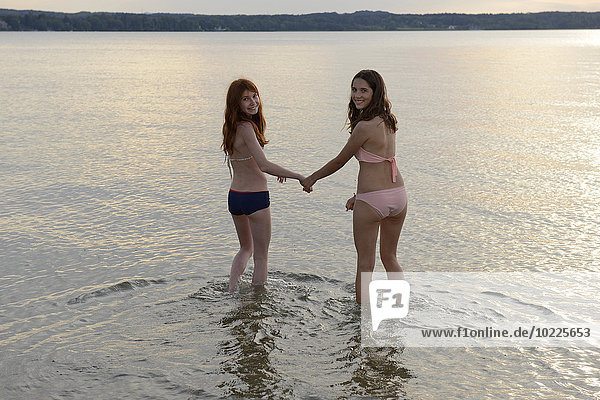 Germany  Upper Bavaria  two girls wading hand in hand in the water of Lake Starnberg