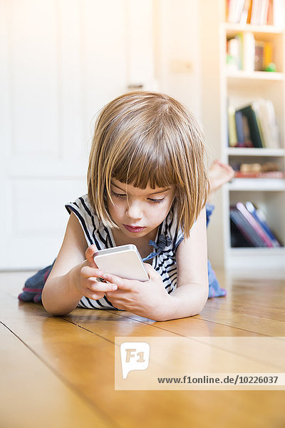 Kleines Mädchen auf Holzboden liegend mit Smartphone