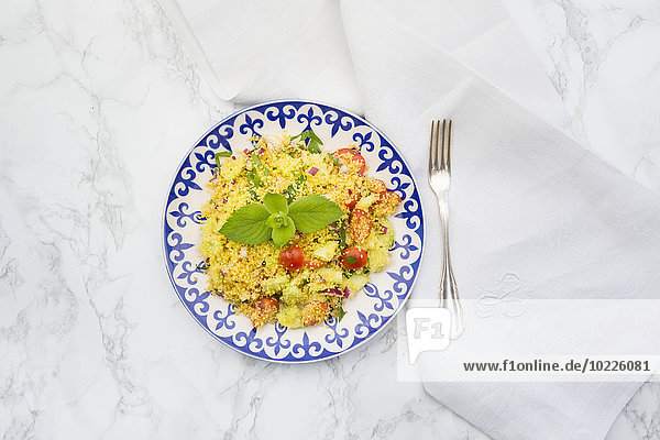 Teller mit Couscous-Salat  Tuch und Gabel auf weißem Marmor