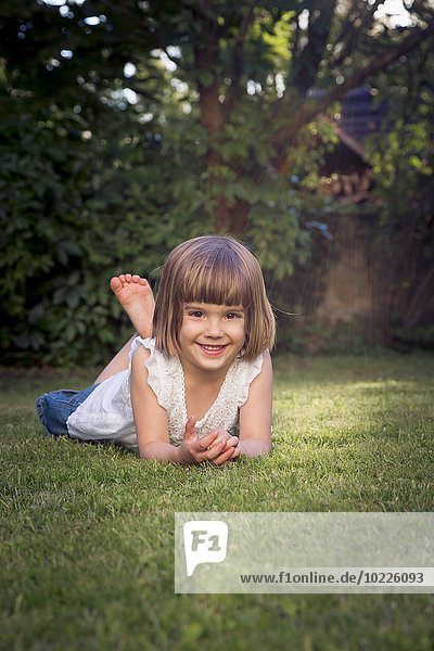 Smiling little girl lying on the meadow in the garden