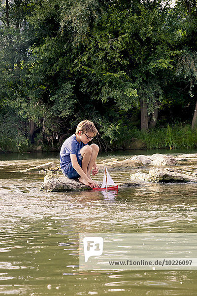 Boy playing with wooden toy boat at a river