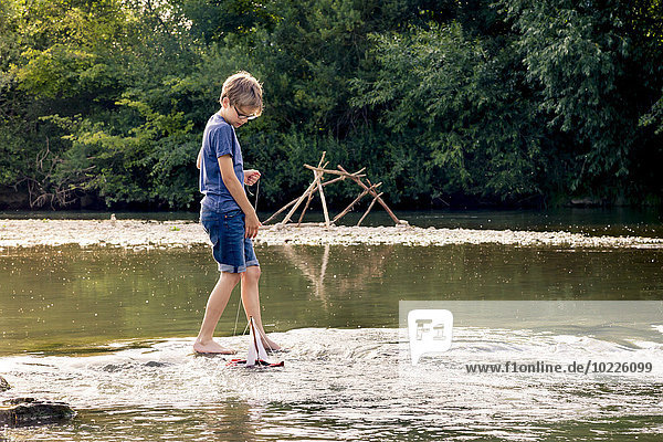 Boy playing with wooden toy boat at a river