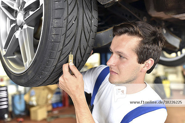 Mechanic measuring tire pattern of a car in a garage