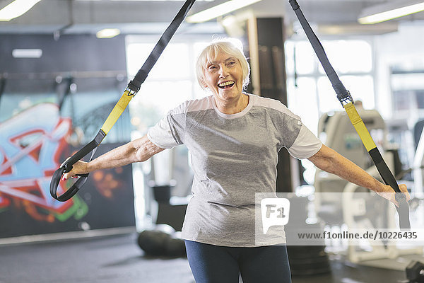 Glückliche Seniorin im Fitnessstudio beim Suspensionstraining