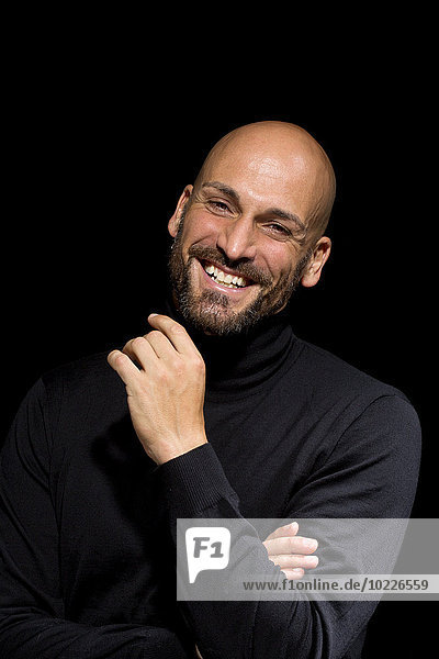 Portrait of laughing man wearing black turtleneck in front of black background