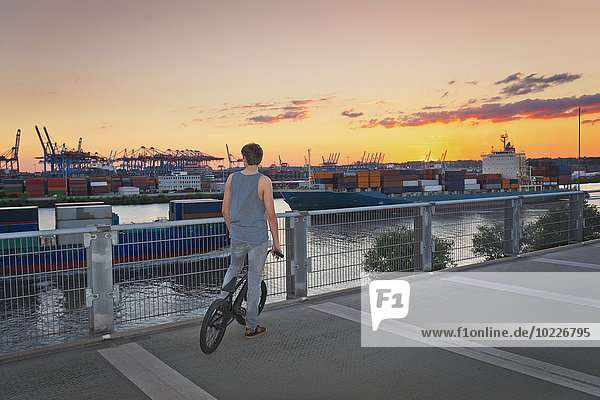 Deutschland  Hamburg  Teenager-Junge steht auf einem Parkplatz und beobachtet Frachtschiffe