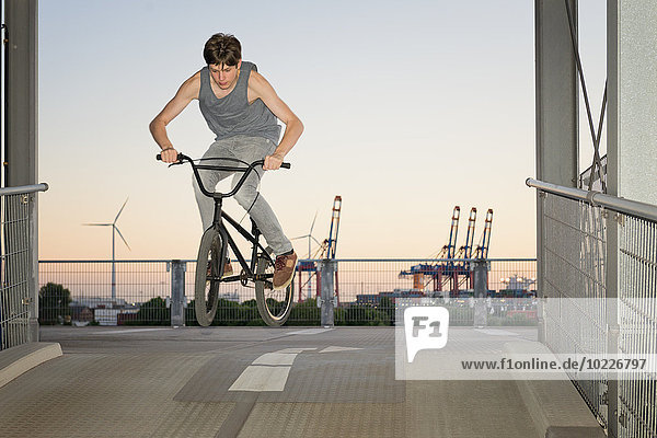 Deutschland  Hamburg  Teenagerjunge springt mit bmx bike auf einer Parkdeckrampe