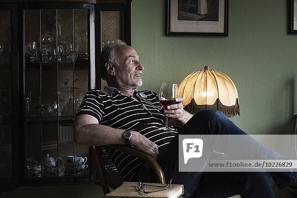 Senior man with glass of red wine relaxing at home