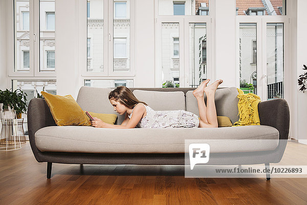 Little girl relaxing with digital tablet on a couch at living room