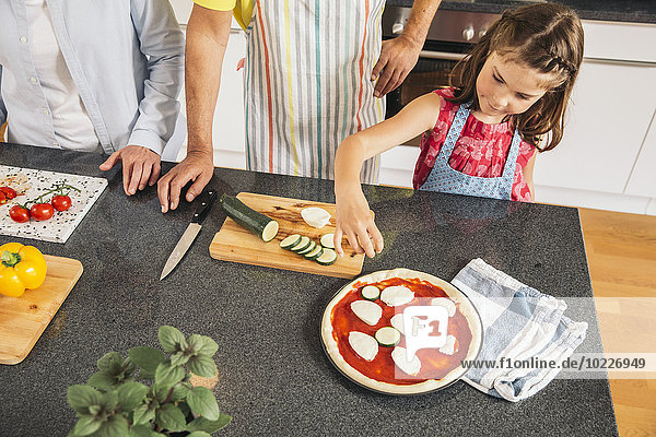 Little girl garnishing homemade pizza in the kitchen