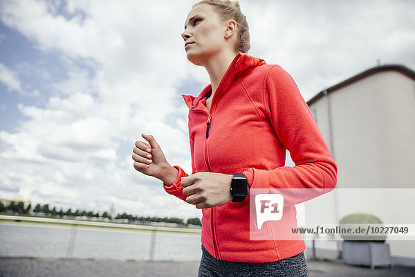 Germany  Cologne  young woman jogging with smart watch