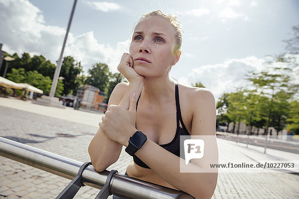 Young sporty woman with smart watch leaning on railing