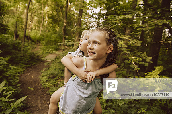 Girl carrying little boy piggyback through a forest