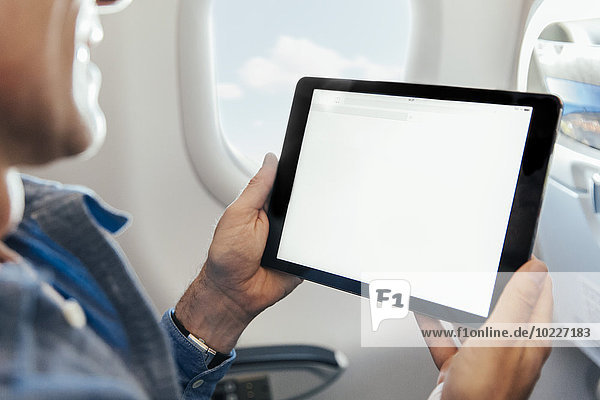 Mann  der auf einem Flugzeug sitzt und ein digitales Tablett hält.