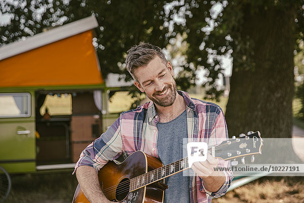 Lächelnder Mann vor dem Van beim Gitarrespielen