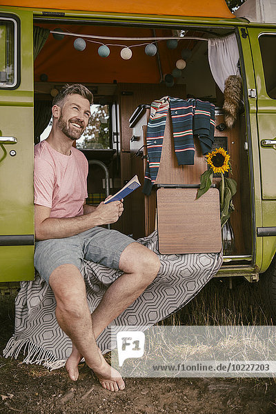 Smiling man reading a book in van