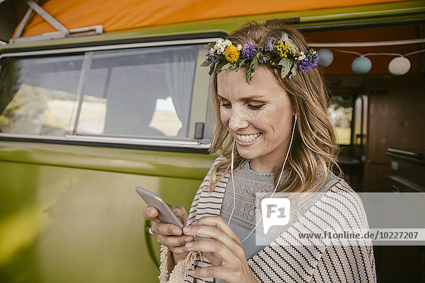 Hippie-Frau hört Musik von ihrem Smartphone vor dem Van
